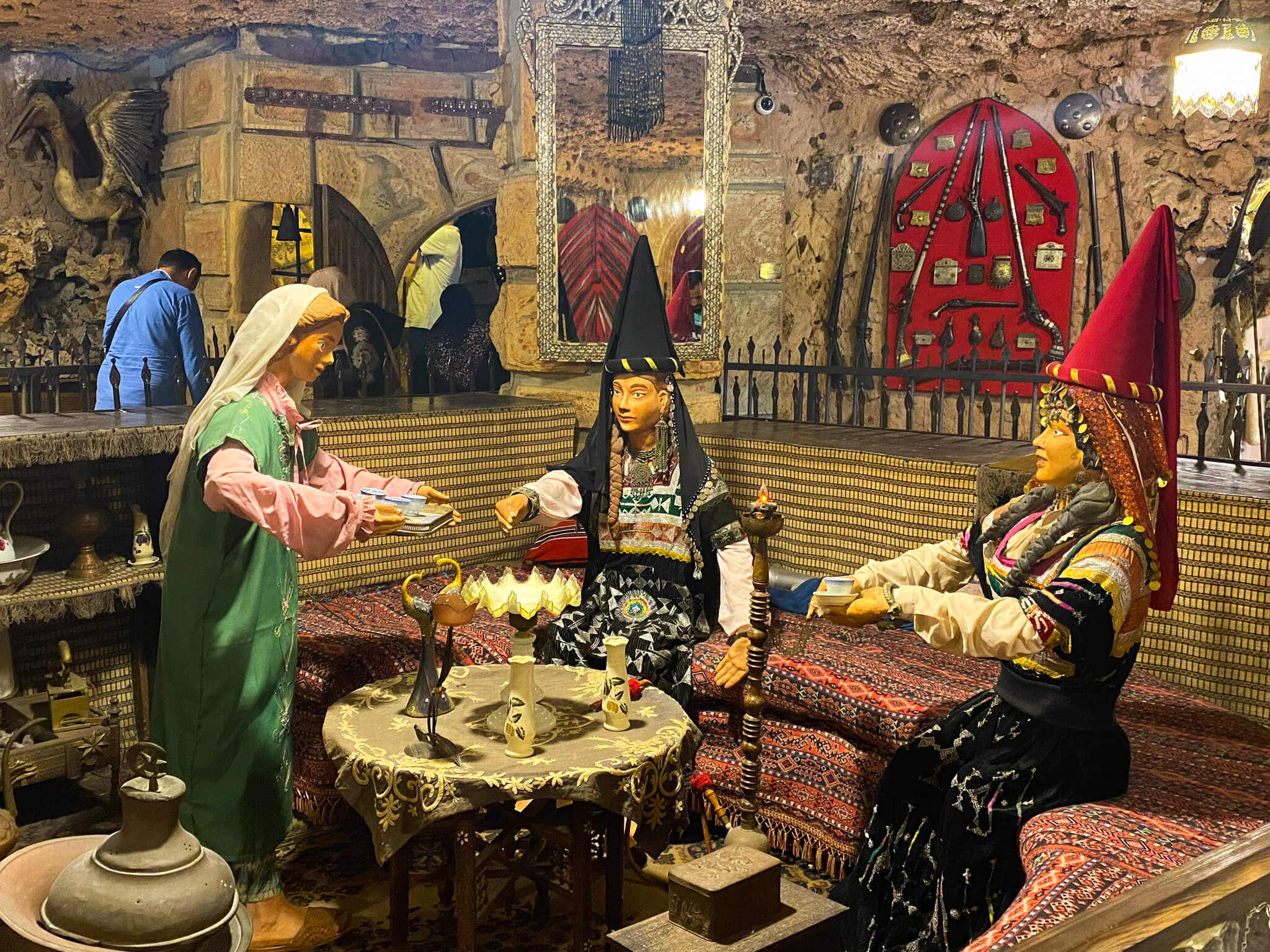 Three mannequins in traditional clothing sit around an old-fashioned table.