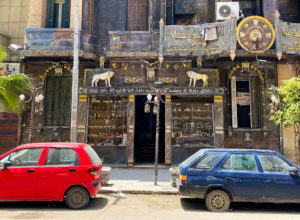 An ornate shopfront on a random street in Alexandria, with two cars parked out front.